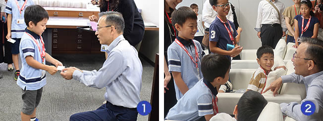 写真1:小さな男の子と社長が名刺交換をしている写真、写真2:社長の椅子に座ったり、椅子の近くで立ったりしている子どもたちと、社長が笑顔で向かい合っている写真